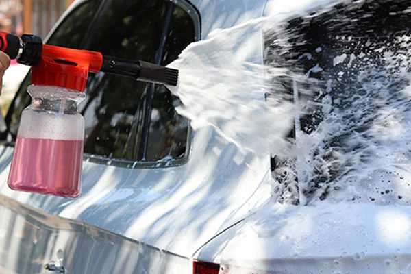 A person using a hose-end foam gun to spray a car