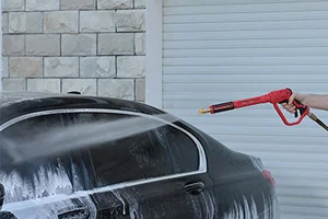 A wide spray of water from a white 40-degree nozzle rinsing soap off a car door