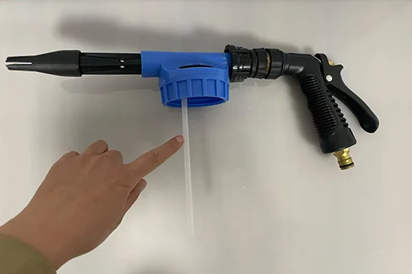 A hand holding the head of a foam gun, pointing to where the siphon tube attaches